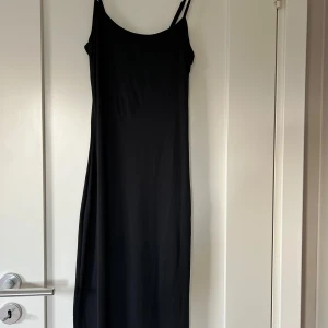 Svart långklänning från NA-KD  - Säljer en svart långklänning från NA-KD i storlek XS. Klänningen har smala axelband och en figurnära passform med enkel, stilren design. Materialet är mjukt och följsamt, perfekt för dig som gillar minimalistisk stil och vill ha en klänning som sitter snyggt.