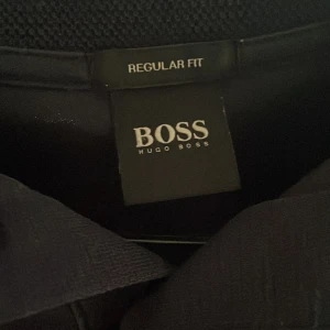 Mörkblå pikétröja från Hugo Boss - Snygg mörkblå pikétröja från Hugo Boss med klassisk krage och korta ärmar. Tröjan har en stilren design utan mönster och är tillverkad i ett mjukt material som känns skönt mot huden. Perfekt för dig som gillar enkel och clean stil.