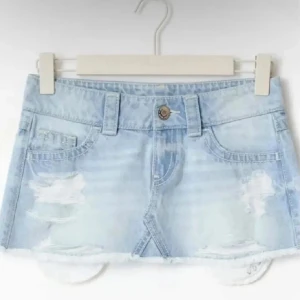 Ljusblå jeanskjol med slitningar - Säljer en ljusblå kort jeanskjol med slitna detaljer och fransad kant. Kjolen har klassiska fickor fram och bak, bälteshällor och knappstängning. Perfekt för dig som gillar en chill och trendig look.