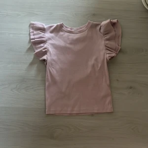 Ljusrosa topp med volangärmar Gina Tricot - Supersöt ljusrosa topp från Gina Tricot med korta volangärmar som ger en extra touch. Toppen har rund hals och är gjord i mjuk bomull. Perfekt för dig som gillar en enkel men ändå trendig look med lite extra detaljer på ärmarna.