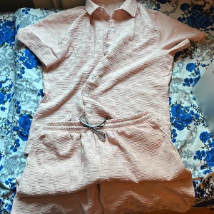 Ljusrosa shorts med strukturmönster - Säljer ett par ljusrosa shorts med snyggt strukturmönster och elastisk midja med snörning. Materialet är mjukt och har en unik textur som ger en cool vibe. Perfekta för varma dagar och chill häng. Färgen är diskret rosa och passformen är loose.