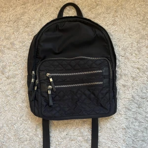 Svart ryggsäck med detaljer - Snygg svart ryggsäck med quiltad framsida och flera dragkedjor med skinndetaljer. Väskan har justerbara axelremmar och praktiska fack framtill samt inne i väskan. Perfekt för dig som vill ha en stilren och funktionell väska! Skriv för fler frågor eller funderingar💕