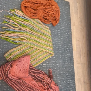 Tre stickade halsdukar i olika färger - Säljer tre halsdukar: en randig i rosa, brun och korall med fransar, en flerfärgad stickad i ljusgrön, blå och beige med långa fransar, samt en orange halsduk med hålmönster. Perfekt för dig som vill ha färg och cool struktur på din look. Pris är per st eller alla för 100kr