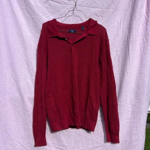 Röd pikétröja från GANT i kashmirmix - Säljer en röd pikétröja från GANT i storlek L. Tröjan har klassisk krage med knapp och är tillverkad i en mjuk mix av bomull och kashmir. Långärmad och med ribbade muddar vid ärmslut och nederkant. Perfekt för dig som gillar stilren och bekväm design.