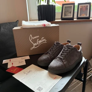 Christian Louboutin skor - Säljer ett par grå sneakers från Christian Louboutin i mjuk mocka med klassisk röd sula och rund tå. Skorna har snörning och neutralt beige foder. Perfekt för dig som gillar exklusiv design och vill sticka ut med Louboutins ikoniska detaljer. Säljer pga tröttnat och kvitto och allt tillbehör följer såklart med! Litet skav framme vid ena skon men inget man ser:) skriv för minsta fundering säljer billigt pga de lilla skavet på ena skon. Pris inte hugget i sten:)