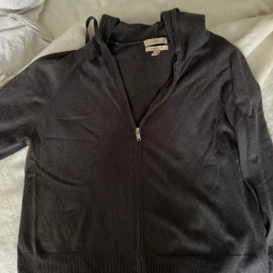Svart hoodie med dragkedja från H&M - Svart hoodie från H&M i kashmirblandning, storlek S. Tröjan har huva, hel dragkedja framtill och långa ärmar. Mjuk och skön känsla med ribbad nederkant och ärmslut. Perfekt för chill dagar eller när du vill ha något bekvämt och stilrent.