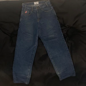 Blå jeans med tryck på bakfickorna - Säljer ett par blå jeans från Junkyard med vitt tryck 'CASH ONLY' på bakfickorna. Med baggy passform och hög midja. Jeansen har även ett ”$” tryck på en av fickorna och kvaliten på jeansen är överraskande bra. Defekterna är streck som skett från invikning av byxorna, strecken går förmodligen att ta bort men det kan vara svårt. Enligt junkyards hemsida är storleken 28. Säljer p.g.a av att jeansen inte är min stil längre. Pris kan diskuteras. 