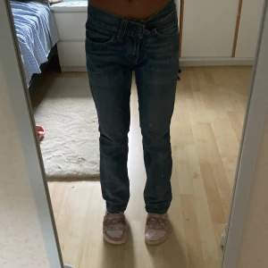 Levi's 501 blå jeans straight fit - Säljer ett par klassiska Levi's 501 jeans i blå tvätt med straight fit. De har låg midja, fem fickor och snygga slitningar för en cool look. Materialet är robust denim i bomull och passformen är normal. Perfekta för dig som gillar tidlös stil och vill ha ett par jeans som alltid funkar.