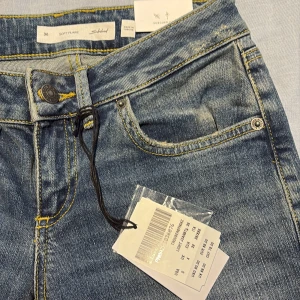 Helt nya!! Blå flare jeans från Subdued, stl xxs (italiensk strl 36) - Supersnygga och helt nya blå jeans från Subdued i modellen Soft Flare, storlek xxs (italiensk 36, europeisk 32).. Jeansen har klassisk femficksdesign, kontrastsydda gula sömmar och coola broderade detaljer på bakfickorna. Materialet är jeans med lätt tvättad look och utsvängda ben för en trendig vibe.