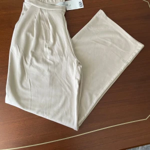 Beige wide byxor från H&M - Snygga beige byxor från H&M med hög midja och breda ben. Tillverkade i mjukt och lätt bomullsmaterial som ger en chill och avslappnad vibe. Perfekta att matcha med sneakers eller sandaler för en clean look.