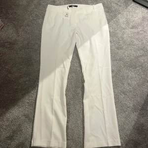 Vita lågmidjade kostymbyxor från Bik Bok - Säljer ett par oanvända lågmidjade vita kostymbyxor från Bik Bok i storlek 42. Byxorna är liten i storleken, raka ben och pressveck framtill. De är tillverkade i ett mjukt material och har hällor för bälte samt diskreta fickor.