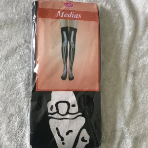 Svarta Halloween knästrumpor med vitt hundmotiv - Säljer ett par svarta knästrumpor från Yem med ett stort vitt hundmotiv framtill. Strumporna är långa och har en cool och lekfull design som sticker ut. Perfekt för dig som vill ha något unikt till din outfit. 