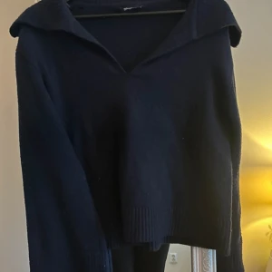 Svart stickad tröja med krage - Säljer en svart stickad tröja med v-ringning och bred krage. Tröjan har långa ärmar och ribbade muddar vid ärmslut och nederkant. Från Gina tricot i storlek S