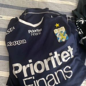 IFK Göteborg fotbollströja från Kappa - Mörkblå IFK Göteborg fotbollströja med vita detaljer och klubbmärke på bröstet. Stora vita tryck med sponsorloggor på framsidan. Klassisk rund halsringning och korta ärmar.