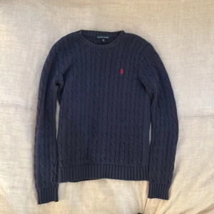 Mörkblå kabelstickad tröja från Ralph Lauren - Säljer en klassisk mörkblå kabelstickad tröja från Ralph Lauren med rund halsringning och röd broderad logga på bröstet. Pris kan diskuteras. Skriv ifall du vill ha fler bilder!