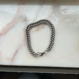 Tjockt silverfärgat armband i kedjemodell - Säljer ett stilrent armband i silverfärgad metall med kraftig kedjelänk. Armbandet har ett klassiskt lås och passar perfekt för att ge en cool touch till din outfit.