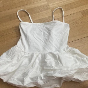 Vit top med volang från H&M Divided - Söt vit top från H&M Divided med smala axelband och volang nertill. Perfekt för varma dagar och enkel att styla med sneakers eller sandaler. Tillverkad i mjukt material för en bekväm känsla.