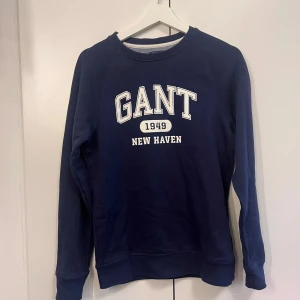 Mörkblå sweatshirt från GANT - Mörkblå sweatshirt från GANT i storlek XS. Tröjan har vit tryckt text framtill med 'GANT 1949 NEW HAVEN'. Klassisk rund halsringning och långa ärmar. 