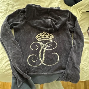 Mörkblå velour hoodie från Juicy Couture - Mysig mörkgrå hoodie i velour från Juicy Couture med glittrande kron- och J-detalj på ryggen. Koftan har dragkedja framtill och huva. Stl S 