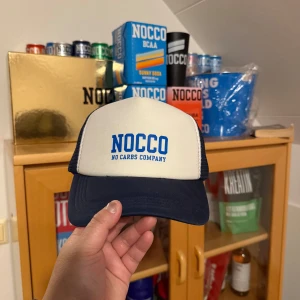 Vit och marinblå keps från NOCCO - Säljer en vit och marinblå keps från NOCCO med blå broderad logga framtill. Kepsen har justerbar baksida i mesh för bra ventilation och passform. Perfekt för dig som gillar sportig stil och vill visa ditt NOCCO-intresse.