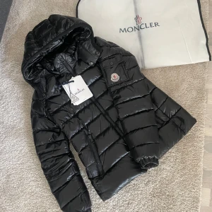 Svart dunjacka från Moncler - Säljer en svart dunjacka från moncler. Använd nu i vinter men säljer den då jag vill köpa en ny. Storlek 1(s) men skulle säga att den passar xs då den är liten i storleken, inget äkthetsbevis förutom qr koden till monclers hemsida, så jag kan inte garantera att jackan är äkta. Köpte jackan begagnad men i nyskick. Kommer med dustbag och lappen. Priset kan diskuteras!