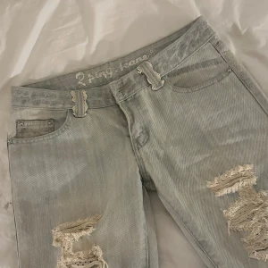 Ljusblå slitna jeans med spetsdetalj - Ljusblå jeans med kraftiga slitningar på benen och en unik spetsdetalj på bakfickan. Jeansen har normal passform och klassisk femficksdesign. Perfekt för dig som gillar en edgy och personlig stil. Perfekt för någon som är kortare!