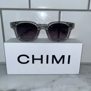 solglasögon från CHIMI model 02 - Snygga solglasögon från CHIMI med transparent båge och mörka glas. Klassisk, rektangulär form som passar de flesta ansikten. Perfekta för att lyfta din stil under soliga dagar. Köpta för 1250kr