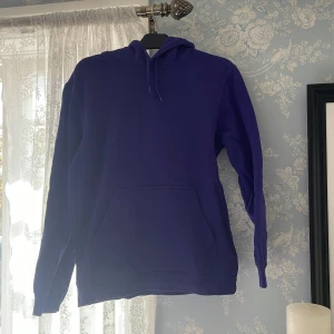 Lila hoodie - Säljer en enkel och stilren mörkblå hoodie med huva och känguruficka framtill. Perfekt för en avslappnad look och passar till det mesta. Mjuk och skön med långa ärmar.