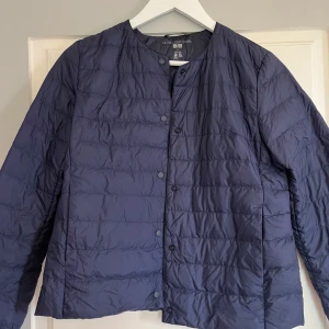 Mörkblå lättviktsdunjacka från Uniqlo - Säljer en mörkblå, tunn och lätt dunjacka från Uniqlo. Jackan har rund halsringning, tryckknappar framtill och är quiltad. Perfekt för lager-på-lager och enkel att bära med sig tack vare sin lätta vikt. Den har använts knappt en gång och är som ny 💓