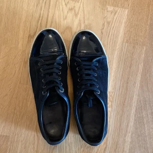 Svarta sneakers från Lanvin med lackad tå - Säljer ett par svarta sneakers från Lanvin med snygg lackad tå och vit sula. Skorna har snörning och är tillverkade i skinn och mocka, vilket ger en lyxig känsla. Perfekta för dig som gillar stilrena och exklusiva sneakers. Storlek 44 men passar även 45. Skicket är bra dom är lite smutsiga på sulan men går lätt att tvätta bort. Pris 2499kr priset är ej hugget i sten