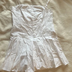 Vit kortklänning med broderade detaljer från Zara - Supersöt vit kortklänning från Zara med tunna axelband och broderade blommor längs sidorna. Klänningen har en lätt utsvängd kjol och är perfekt för varma dagar. Materialet känns svalt och luftigt. Jag kommer såklart stryka den när jag skickar klänningen!