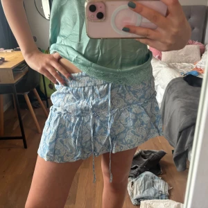 Blå  vit mönstrad kjol med volanger från Zara - Supersöt  blåvit mönstrad kortkjol med  och volangkant. Kjolen har resår i midjan och knytband framtill för extra passform. Perfekt för varma dagar och ger en fräsch look. Sparsamt använd, så nästan i nyskick!