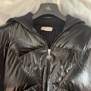 Svart cardigan från Moncler - Säljer min svarta Moncler-jacka med glansig framsida i syntet och stickade ärmar och rygg. Jackan har dragkedja framtill och Moncler-logga på ärmen. Aldrig använt 