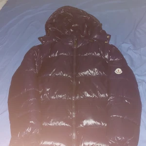 Mörkblå dunjacka från Moncler - Säljer en mörkblå glansig dunjacka från Moncler med huva och dragkedja. Jackan har Moncler-logga på ärmen och klassisk pufferdesign. Perfekt för kyliga dagar och riktigt snygg till streetwear-stil. Pris kan diskuteras.