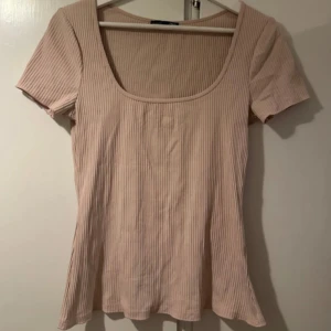 Ljusbeige ribbad topp med kort ärm - Säljer en ljusrosa ribbad topp med korta ärmar och djup rundad urringning från Zara.Toppen har en väldigt fin passform som är lätta att styla. Den kommer inte till användning då den bara ligger i garderoben så därför säljer jag denna. Frakten betalar man för själv 