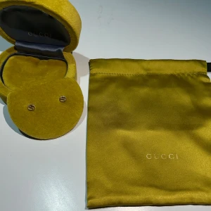 Guldiga örhängen från Gucci - Säljer ett par eleganta guldiga örhängen från Gucci. Kommer i original gul sammetsask och matchande tygpåse med Gucci-logga. Perfekt accessoar för att lyfta din stil.