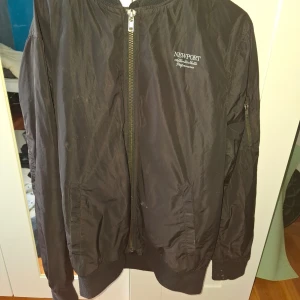 Svart bomberjacka från Newport - Säljer en svart bomberjacka från Newport i storlek L. Jackan har dragkedja framtill, ribbade muddar vid ärmslut och nederkant samt fickor på sidorna. Klassisk och stilren design med diskret logga på bröstet.