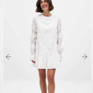 Nakd vit klänning med öppen rygg - Superfin vit klänning med blommigt broderi, volang nertill och långa puffärmar. Klänningen har öppen rygg med knytband och är i ett lätt, luftigt material. Perfekt för sommarens alla tillfällen! Perfekt dom studenrklänning