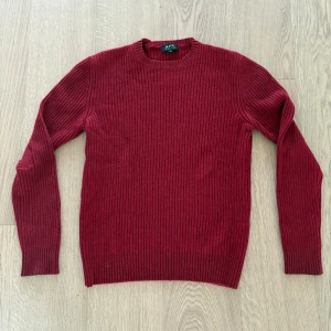 Vinröd stickad tröja från A.P.C. - Säljer en vinröd stickad tröja från A.P.C. i storlek M. Tröjan har rund halsringning och ribbstickat mönster över hela plagget. Perfekt för kyligare dagar och enkel att matcha med olika outfits.