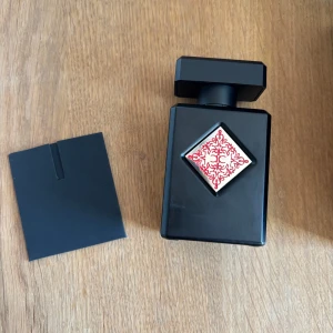 Initio Absolute Aphrodisiac  - Lyxig parfym från Initio i en svart, fyrkantig flaska med en röd dekorativ detalj på framsidan. Kommer i en elegant svart kartong med samma röda mönster. Flaskan rymmer 90 ml och är en Eau de Parfum. Kvitto följer med 