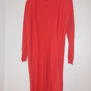 Orang  lång kofta från Esmara - Säljer en röd lång kofta från Esmara. Koftan är öppen framtill, har lång ärm och är tillverkad i ett mjukt, stickat material. Perfekt att slänga över en topp för en färgklick i vardagen.