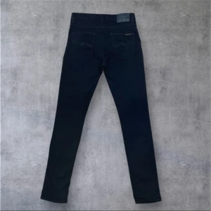 Svarta jeans från Nudie Jeans - Säljer ett par svarta jeansbyxor från Nudie Jeans med klassisk femficksdesign och silverfärgade nitar. Byxorna har rak passform och normal midja, tillverkade i ett mjukt bomullsmaterial. Perfekta för en stilren look. Hör av dig vid frågor eller pris förslag 