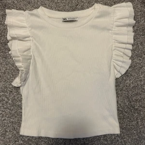 Vit ribbad topp med volangärmar från Zara - Supersöt vit ribbad topp från Zara med volangdetaljer på axlarna. Används inte längre då den är lite för liten💕(priset går att diskuteras) 