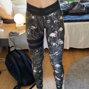 Svarta träningstights med flamingomönster från Stronger - Snygga svarta träningstights från Stronger med tropiskt mönster och vita flamingos. Två svarta ränder på ena benet. Perfekta för gymmet eller yoga. Stretchigt material som sitter skönt på kroppen. Köpt för 899 kr!