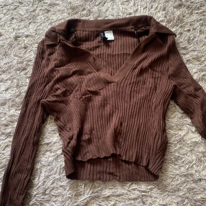 Brun ribbad croppad tröja med v-ringning - Säljer en brun ribbad croppad tröja med v-ringning och långa ärmar. Tröjan har en snygg krage.💖