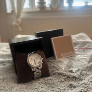 Silverfärgad klocka från Michael Kors - Stilren klocka från Michael Kors i silver med länkarmband och flera urtavlor. Klockan levereras i originalask med extra länkar och manual. Perfekt accessoar för dig som gillar klassisk design och detaljer. Kan minskas/göras större.  Jag har även kvittot!