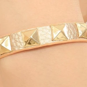 Guldarmband med nitar - Snyggt armband i guld med stora pyramidformade nitar. Armbandet har en bred rem i syntetmaterial och ger en cool och trendig look. Perfekt accessoar för att lyfta din outfit.