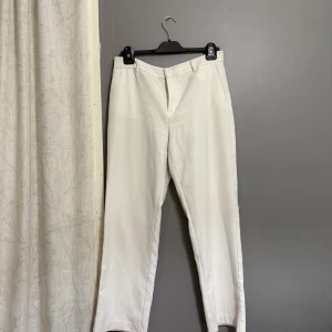 Vita kostymbyxor från Gina Tricot - Snygga vita kostymbyxor från Gina Tricot med klassisk passform och raka ben. Byxorna har diskreta fickor och hällor för bälte, perfekta för en clean och stilren look.