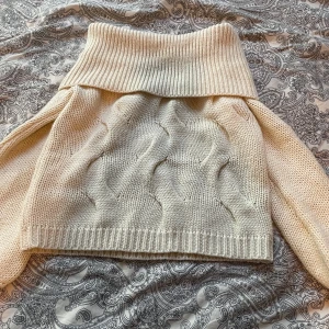 Beige stickad polotröja med mönster - Säljer en beige stickad polotröja med bred polokrage och snyggt vågigt mönster framtill. Tröjan har långa ärmar och ribbade muddar. Perfekt för kyliga dagar och enkel att styla till olika outfits.