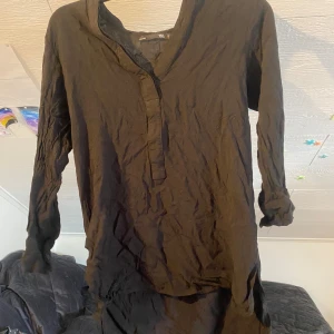 Svart lång skjorta från 157 - Svart lång skjorta från 157 i enkel och avslappnad modell med v-ringning och långa ärmar. Tillverkad i ett lätt och mjukt material som känns skönt mot huden. Perfekt för dig som gillar minimalistisk stil.